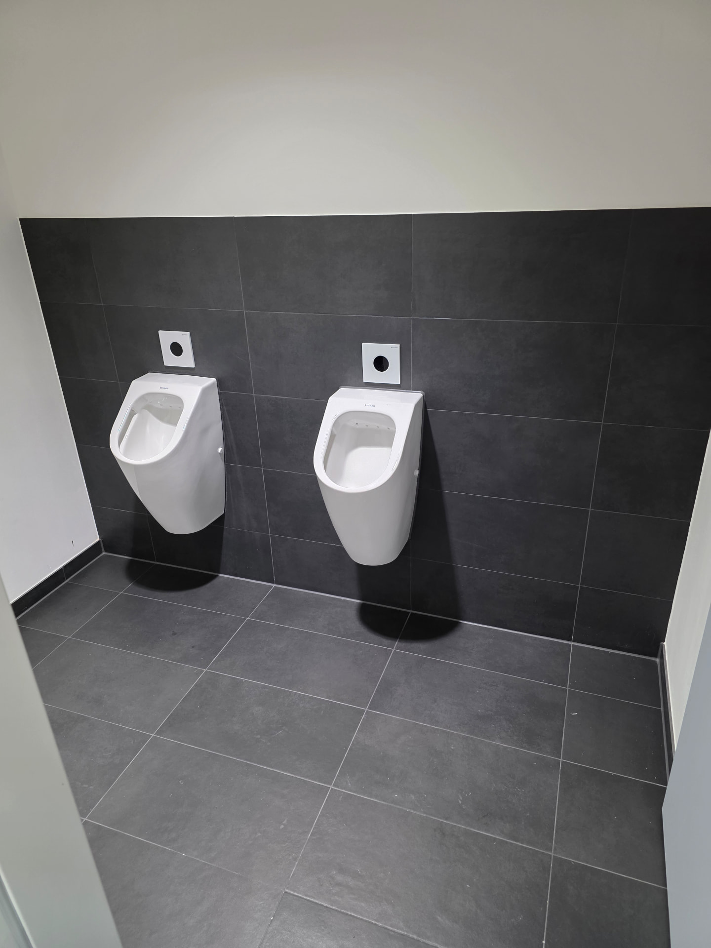 Geflieste Urinalanlagen bei Rohde & Schwarz in München mit anthrazitfarbenen Wand- und Bodenfliesen